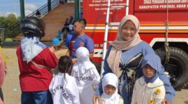 WALAUPUN MEMBELUDAK TETAP AMAN: Seorang ibu, Cika Nabila, bersama anak-anaknya berfoto di depan armada Damkar PALI saat mengantre wahana Flying Fox gratis dalam momen Sunday Morning di Lapangan Sanggar Pramuka Gelora November Pertamina Pendopo, Talang Ubi, Minggu (7/6/2026). Wahana edukasi adrenalin ini sukses menyedot perhatian ratusan warga dengan pengawasan ketat personel Damkar demi menjaga komitmen 'Zero Accident'. (Foto: Dok/tintamerah.co)