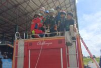 Petugas Damkar PALI dengan sigap memasang tali pengaman (harness) pada anak-anak warga di atas mobil rescue "Challenger" dalam wahana Flying Fox gratis di Lapangan Tribun Gelora November Pertamina Pendopo, Talang Ubi, PALI, Minggu (7/6/2026). Momen ini diwarnai kegaduhan jenaka dari sepasang anak kembar Reno, di mana sang adik (tengah) tampil sangat berani dan heboh menantang ketinggian, sementara sang kakak (kanan, kaos hitam berpaling) tampak dilingkupi rasa takut dan memilih mundur dari peluncuran ekstrem tersebut. (Foto: Dok/tintamerah.co)
