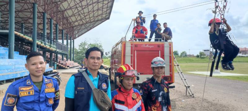 Kepala Bidang Penanggulangan Kebakaran dan Penyelamatan Dinas Damkar PALI, Suyadi (kedua dari kiri, rompi biru), saat diwawancarai oleh wartawan tintamerah.co di sela-sela memantau jalannya wahana flying fox gratis di Lapangan Tribun Gelora November Pertamina Pendopo, Talang Ubi, Minggu (7/6/2026). Suyadi menegaskan pelaksanaan kegiatan mengutamakan keselamatan penuh (zero accident) sesuai instruksi pimpinan, sekaligus mengevaluasi masukan warga untuk pengembangan kegiatan ke depan.  (Foto: Dok/tintamerah.co)